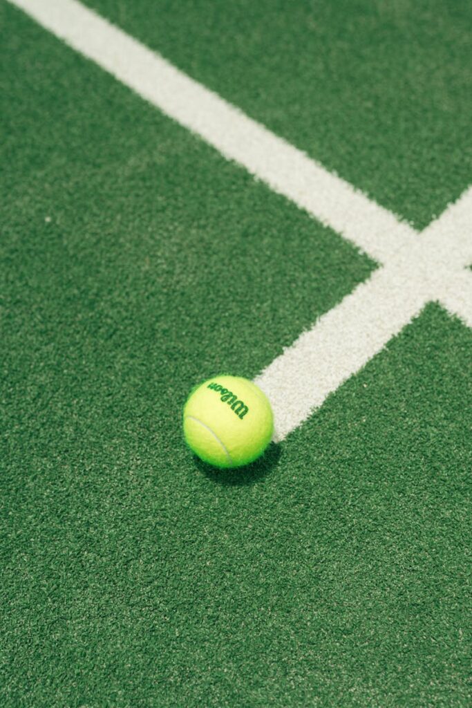 Close-up of a tennis ball on a green court with white lines, outdoor sports theme.